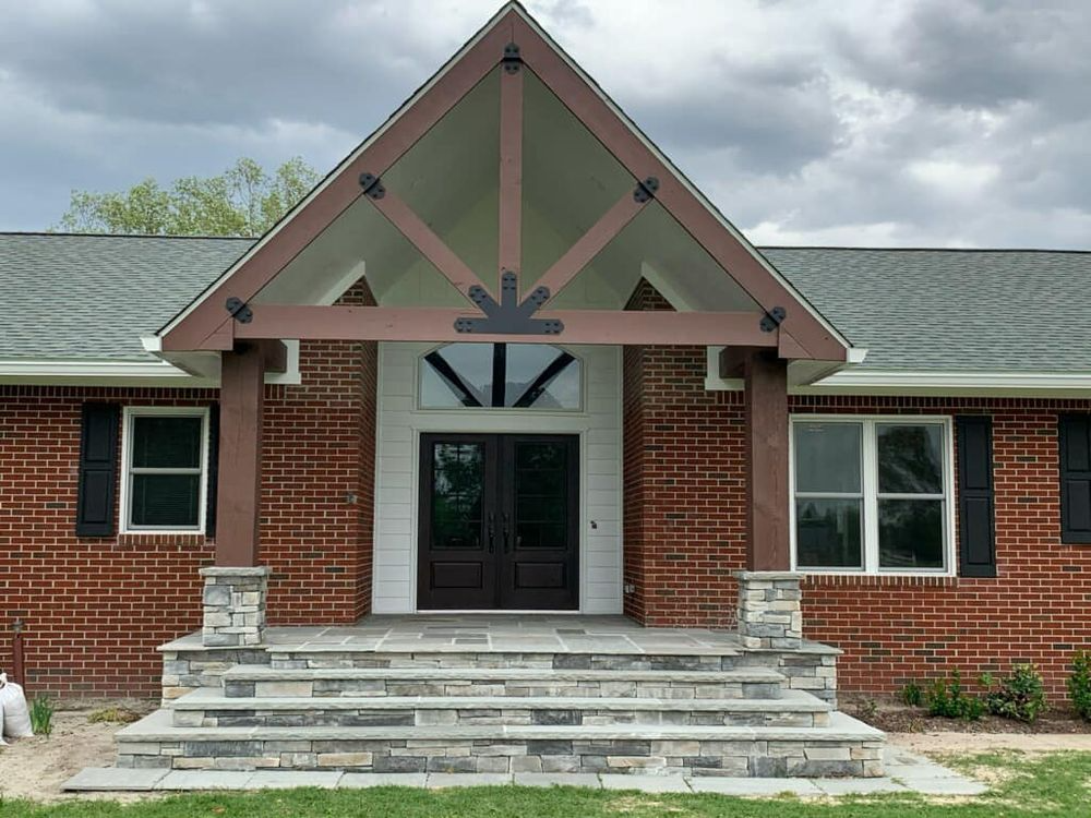 Brick house with stone steps, a brown wooden portico, and black doors. Cloudy sky.