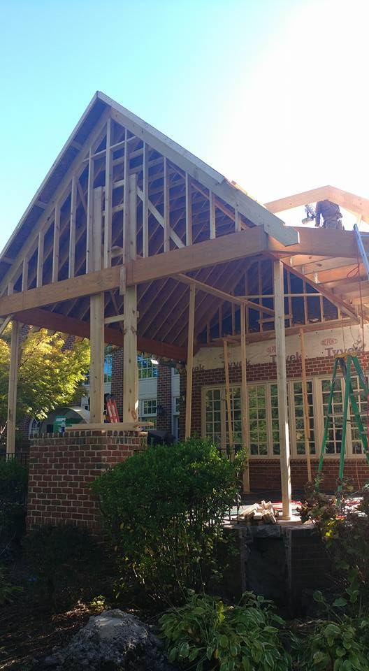 Framed wooden structure of a house under construction; brick, window openings, and clear sky.
