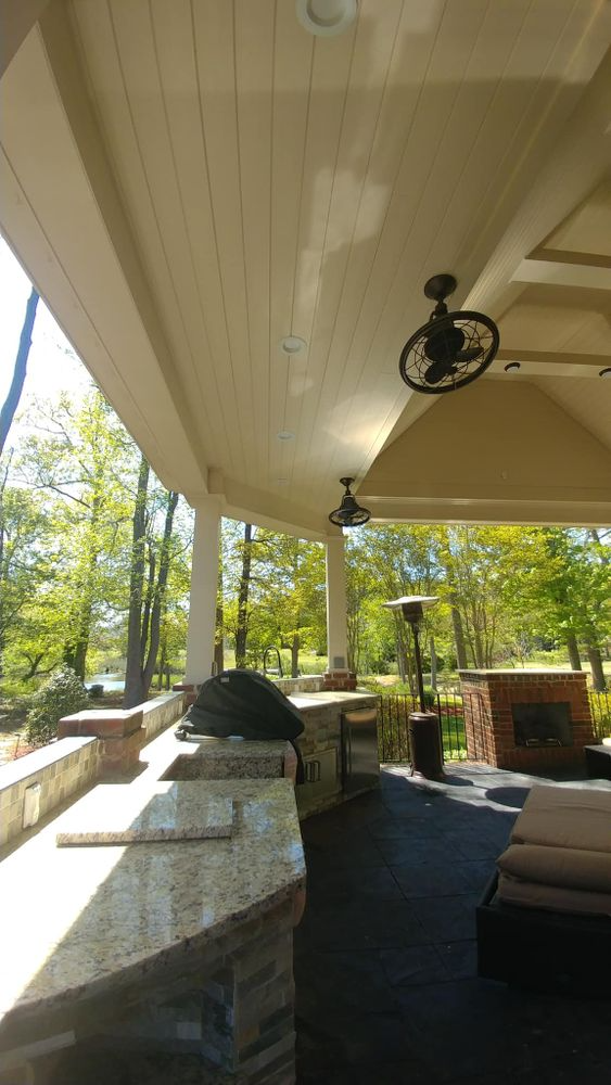 Covered outdoor patio with kitchen, fireplace, ceiling fans, and a view of trees.