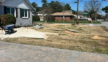 Front yard undergoing landscaping; house, street, grass, sand, and wood visible.