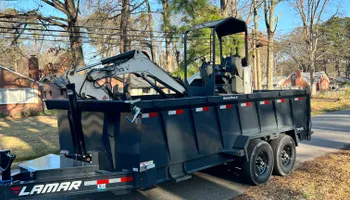 Black dump trailer with attached backhoe parked on a residential street.