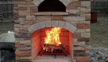 Stone outdoor fireplace with a fire burning inside.