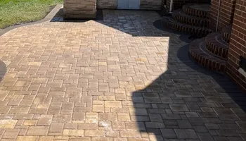 Brick patio with a curved border, adjacent to grass and a brick house.