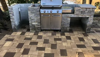 Outdoor kitchen with stainless steel grill, stone facade, and patterned brick patio.