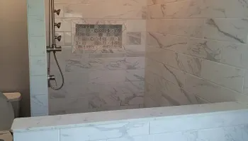 A white marble tiled shower with built-in shelves and a multi-head shower system.