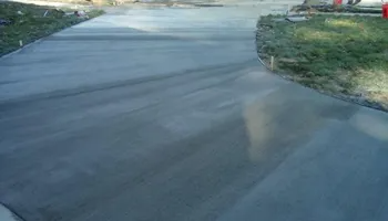 Newly poured concrete driveway, curving toward grass. Light gray surface reflects sunlight.