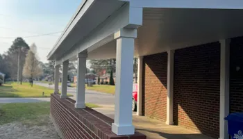 Covered porch with white columns and red brick, looking down a street.