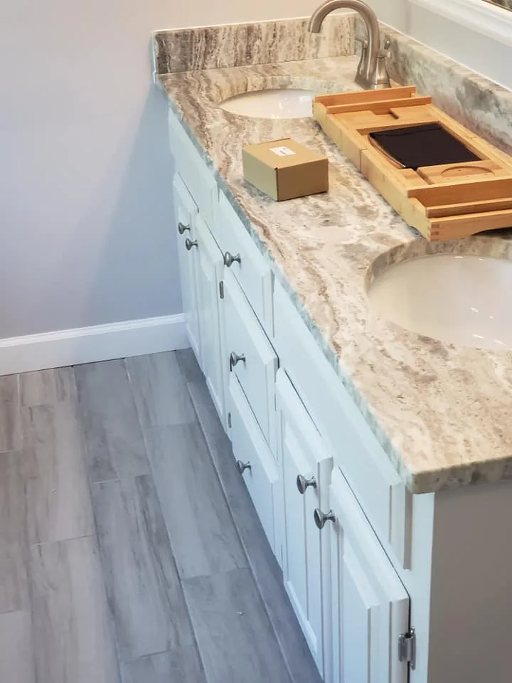 White bathroom vanity with marble countertop and two sinks, with gray tile flooring.