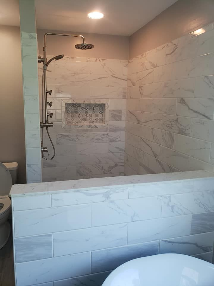 Spacious bathroom with marble tile shower and built-in shelf. Silver shower fixtures and white toilet visible.