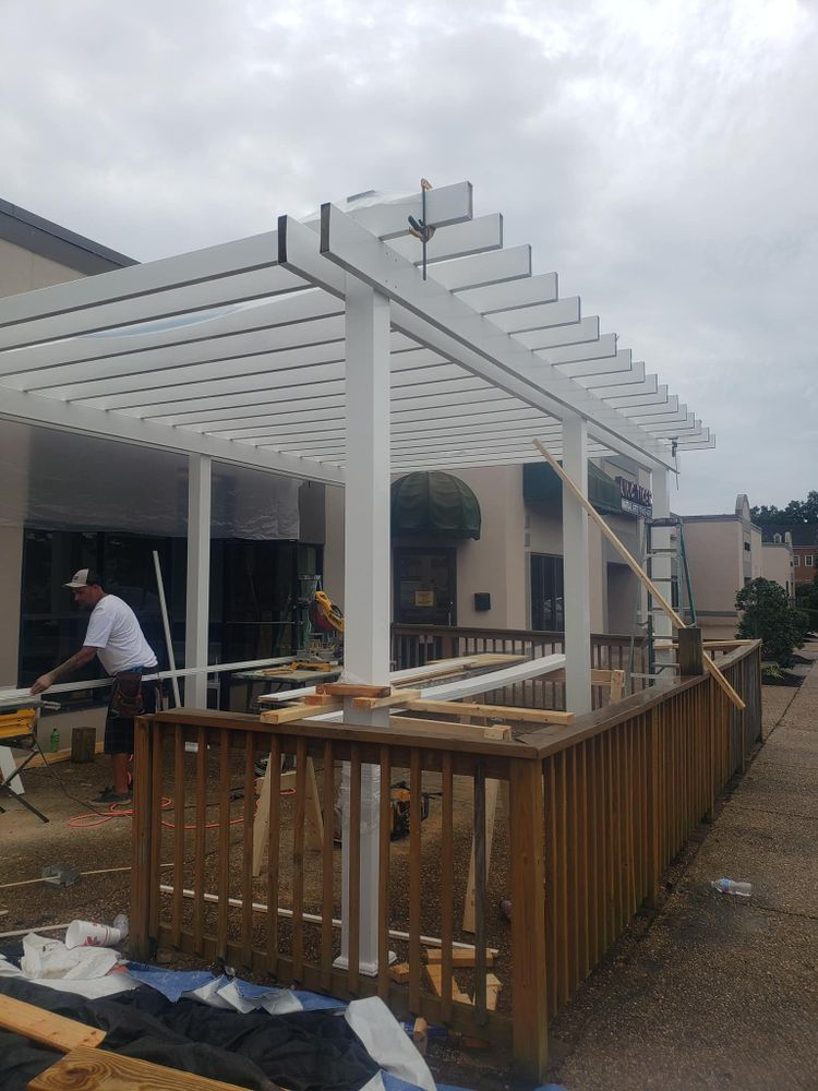 Workers constructing a white pergola over a wooden deck attached to a building.