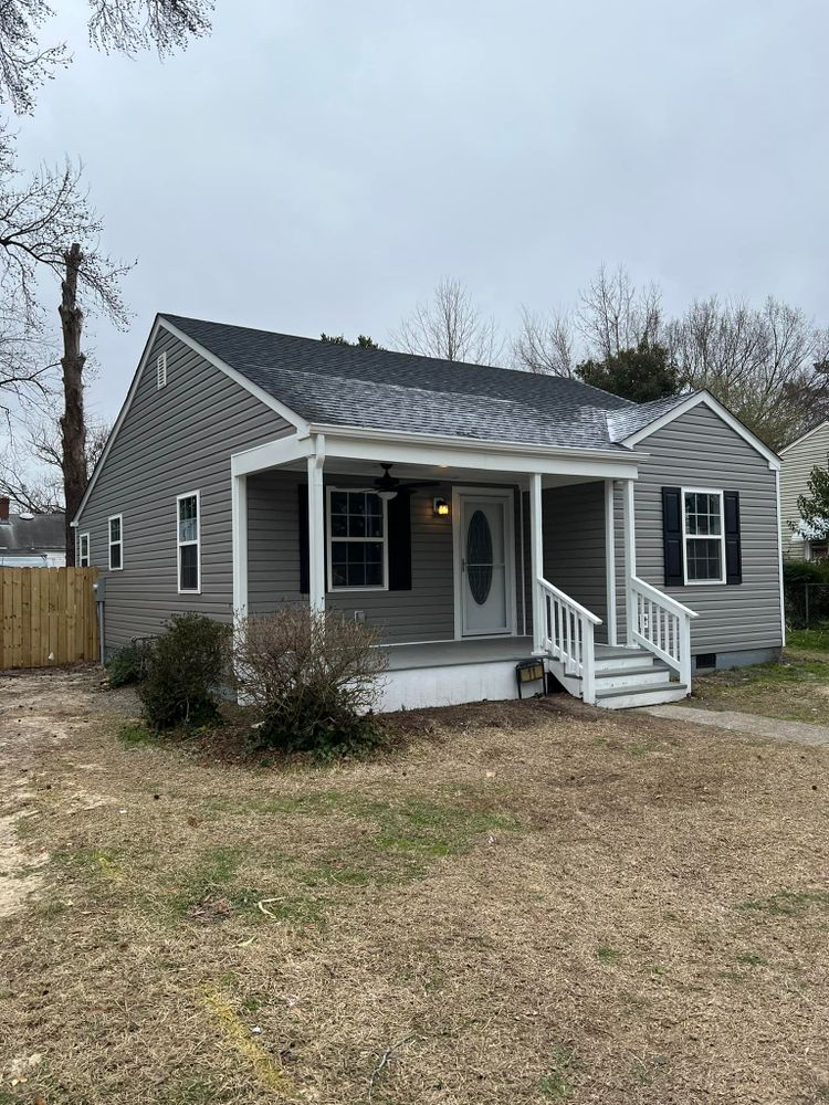 Gray house with white porch and shutters, small front yard, cloudy day.