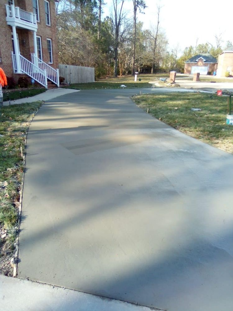 Newly poured concrete driveway leading to a brick house. Green grass borders the driveway.