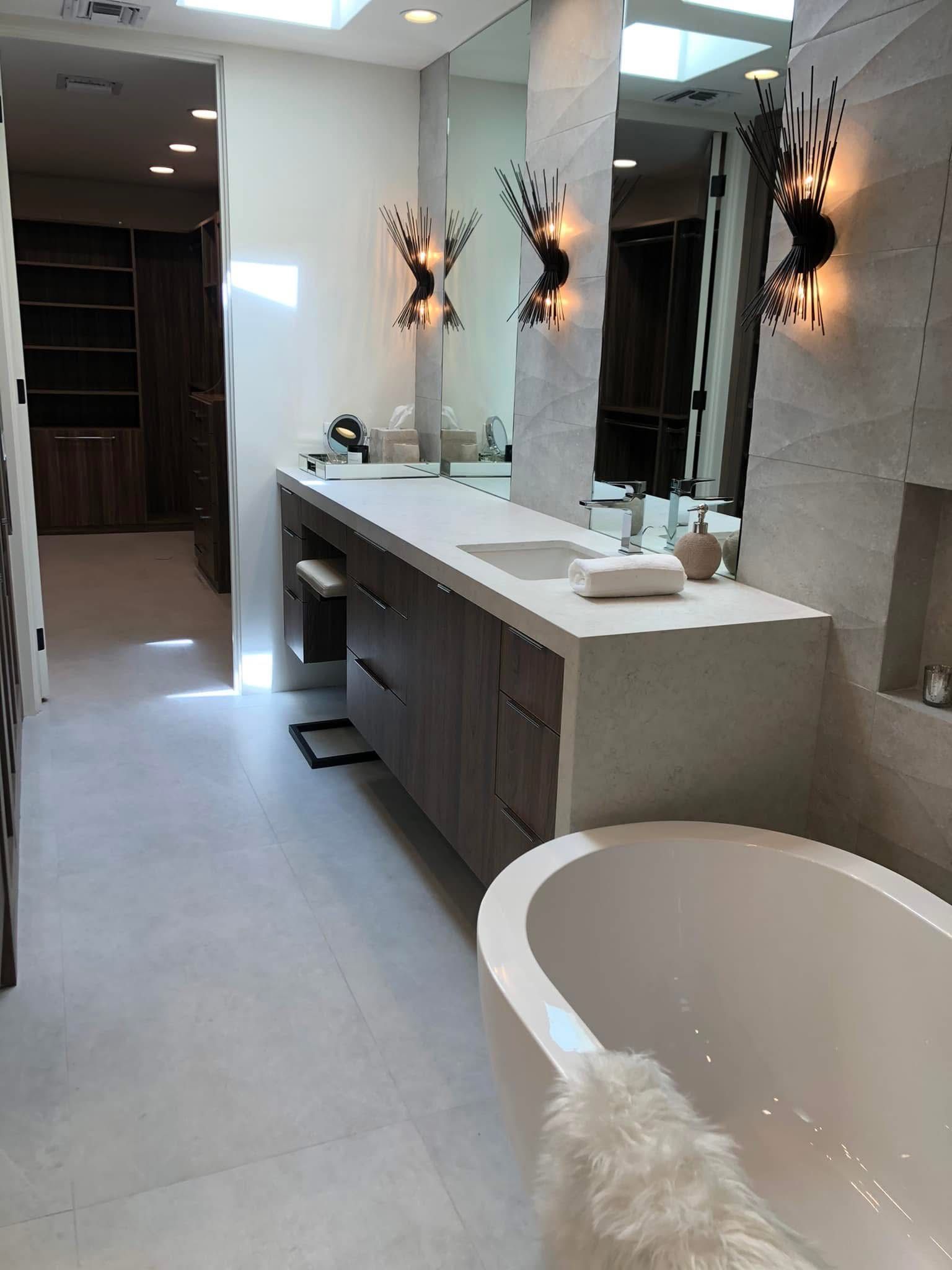 Modern bathroom with double vanity, large mirrors, wall sconces, and a freestanding tub at right.