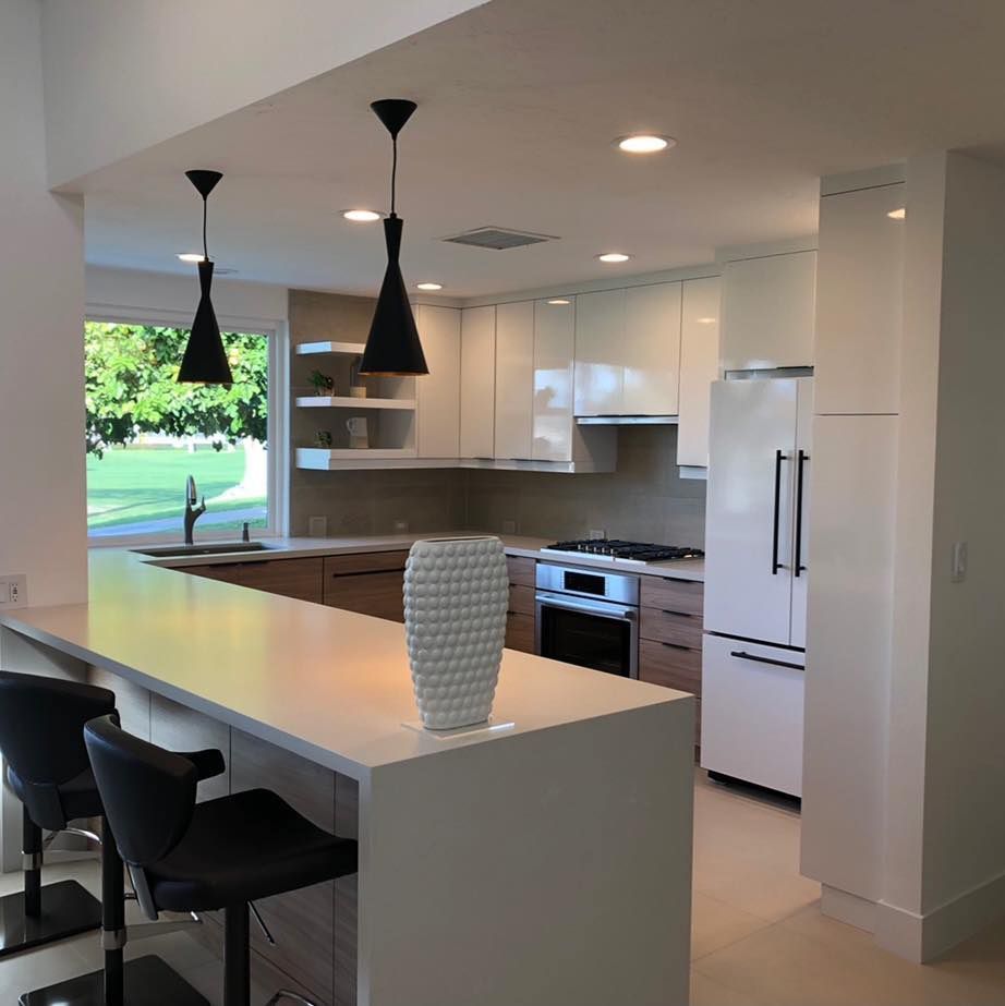 Modern white kitchen with island, black pendant lights, stools, and a view of greenery outside