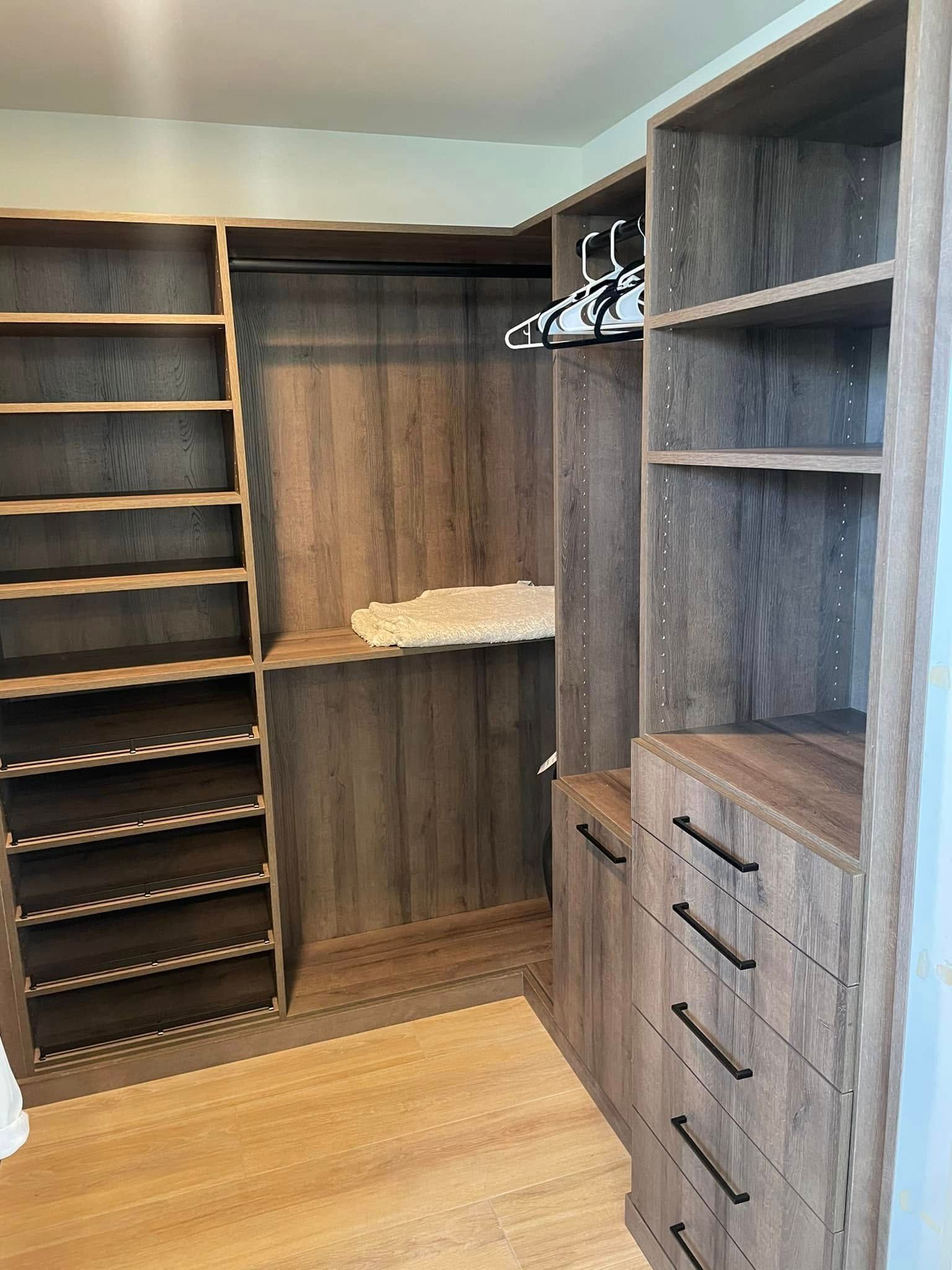 Walk-in closet with dark wood shelving, hanging rods, and built-in drawers on light wood floor