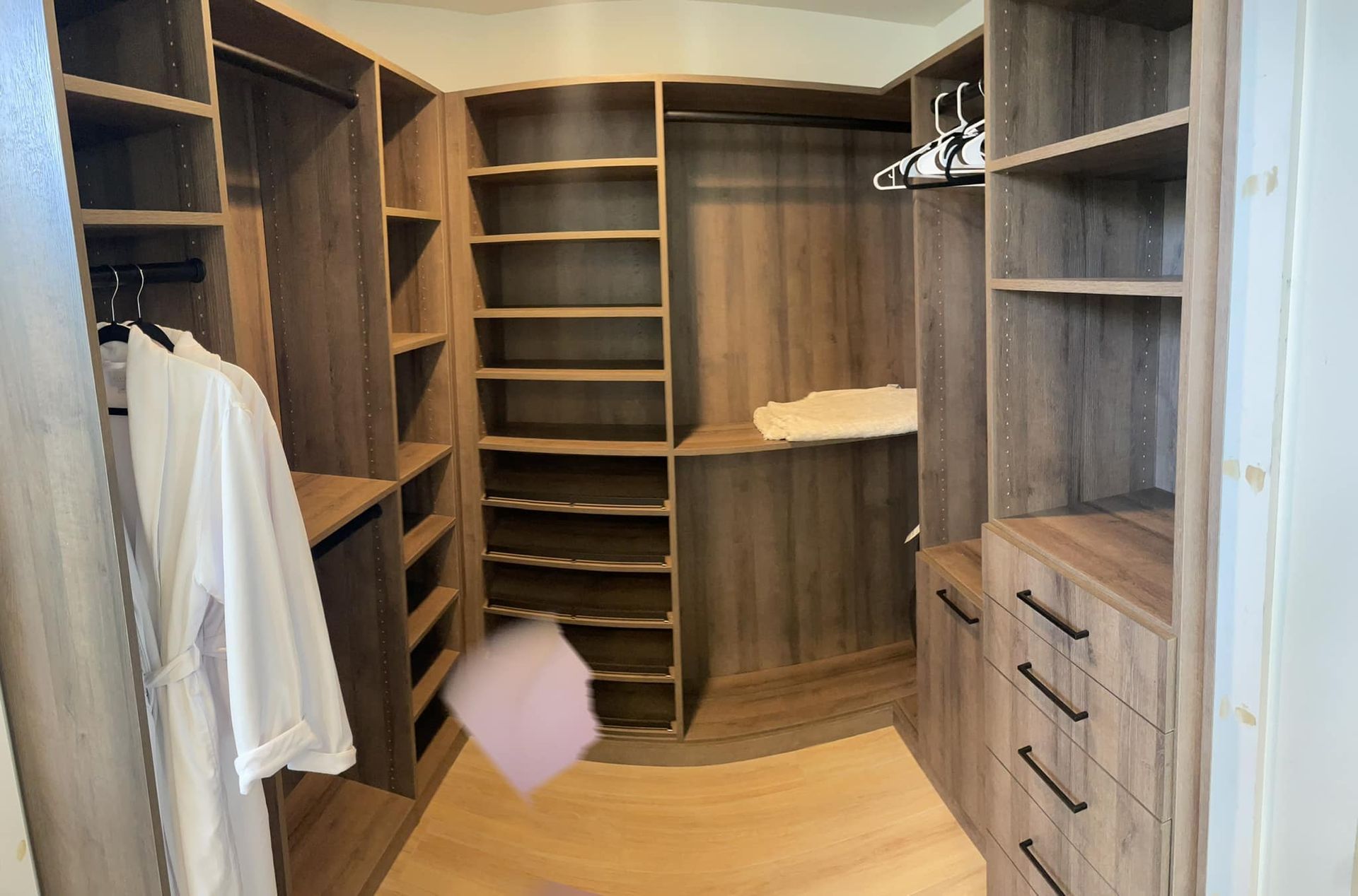 Spacious walk-in closet with wooden shelving, drawers, hanging rods, and light wood flooring.
