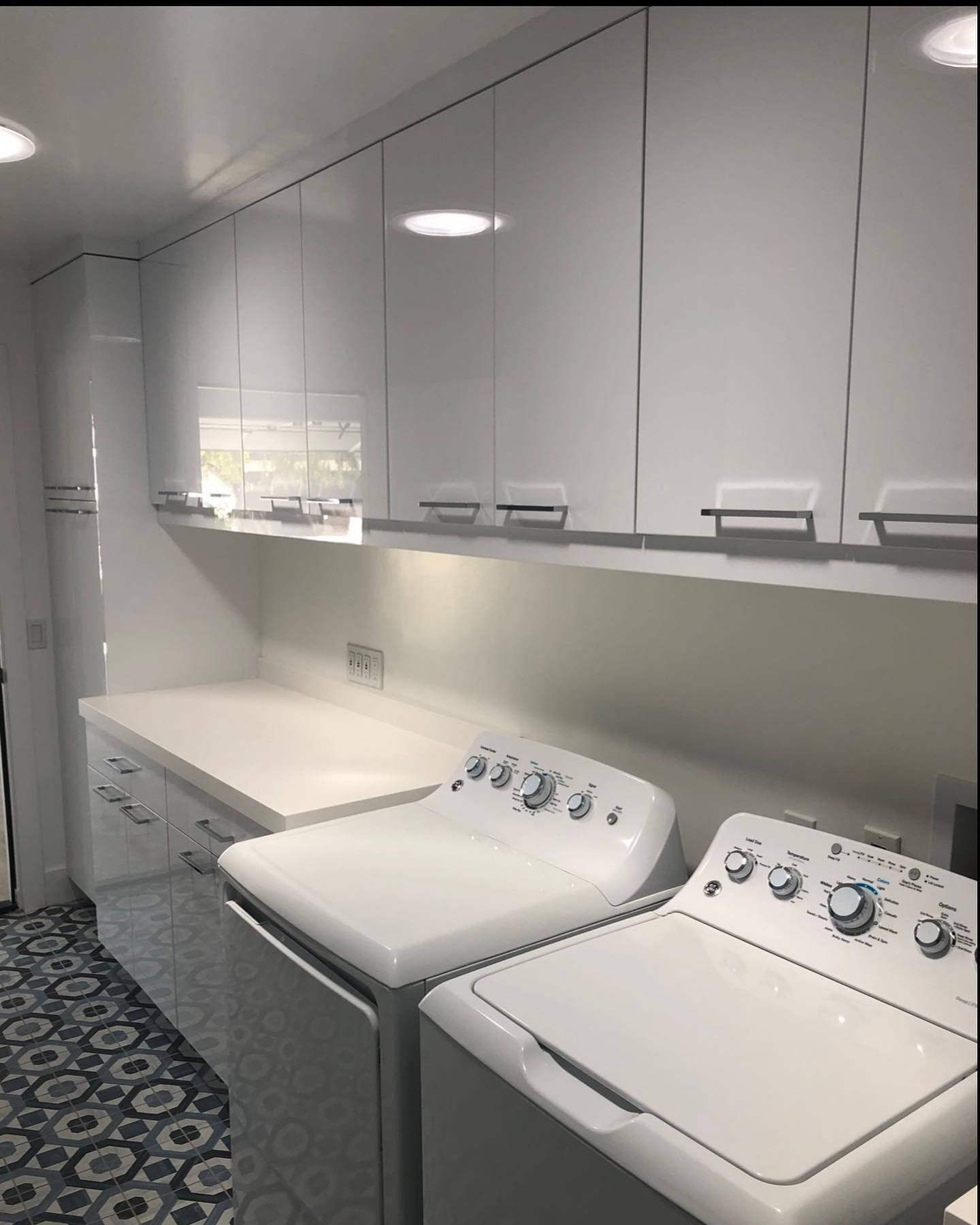 Bright laundry room with white cabinets, countertop, and two front-loading washer/dryers.