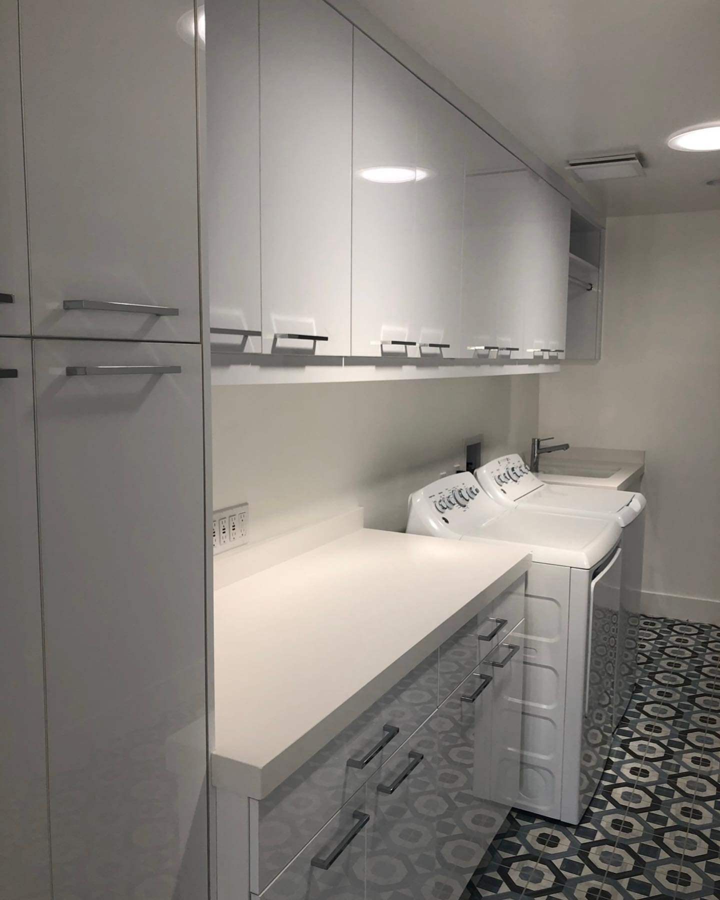 Small laundry room with white cabinets, countertop, sink, and patterned tile floor.