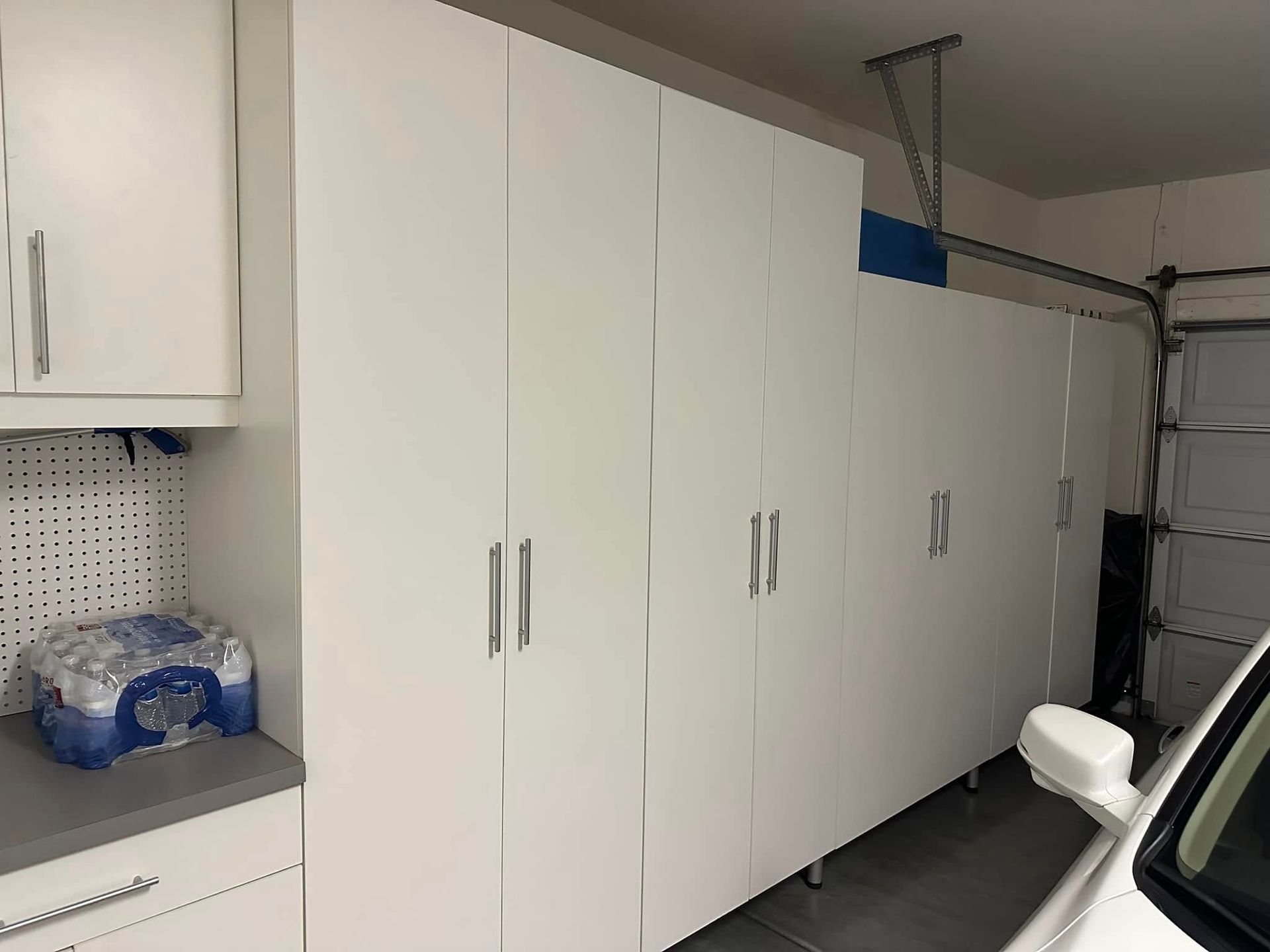 White storage cabinets and a workbench in a garage, with a folded chair in the foreground.