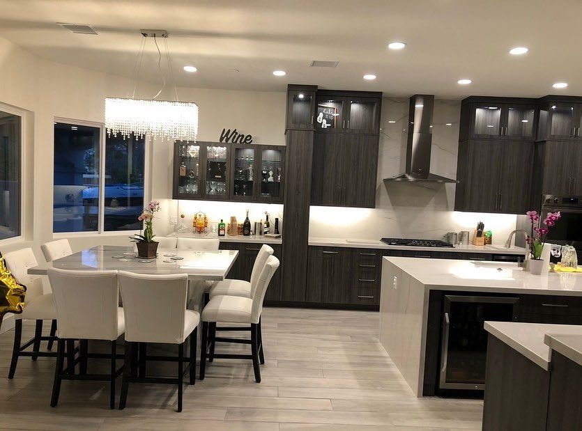 Modern open-concept kitchen and dining room with white chairs, dark cabinets, and pendant lighting