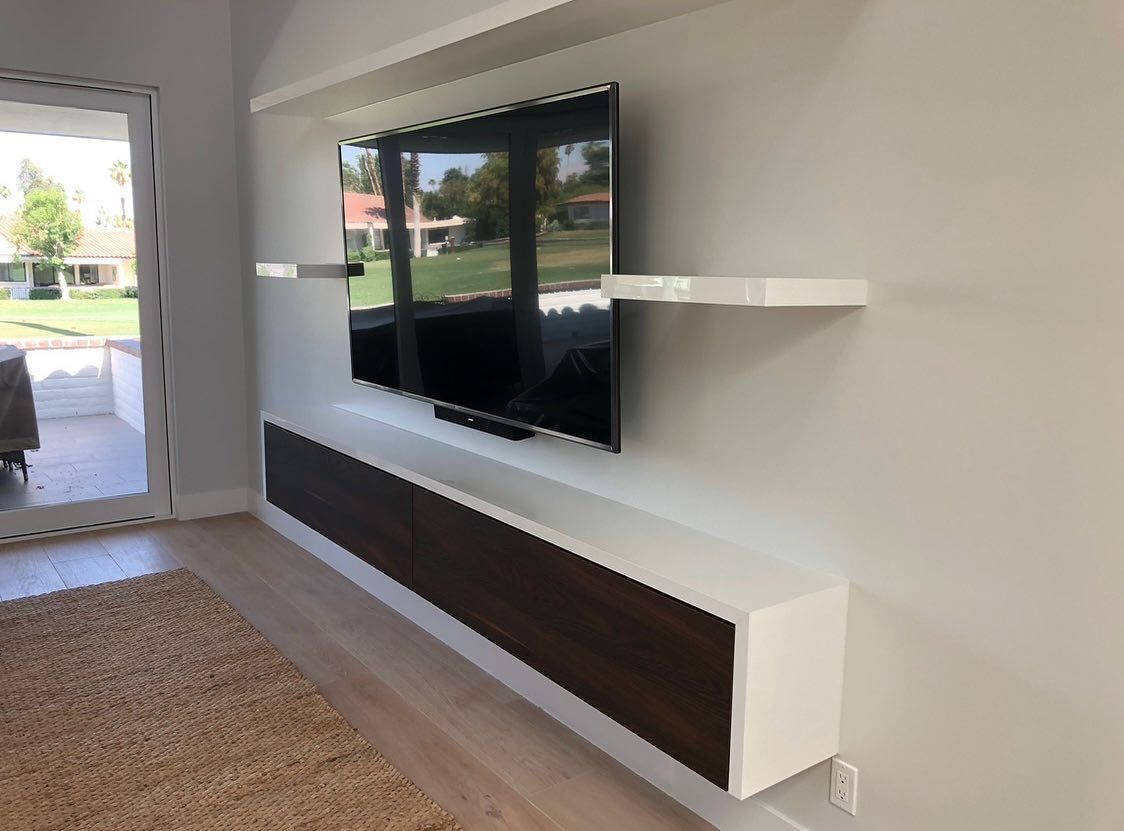 Modern living room with wall-mounted TV, white shelves, and a long floating cabinet by a glass door