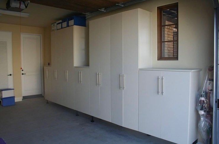 Row of white storage cabinets in a garage with a beige door and gray floor