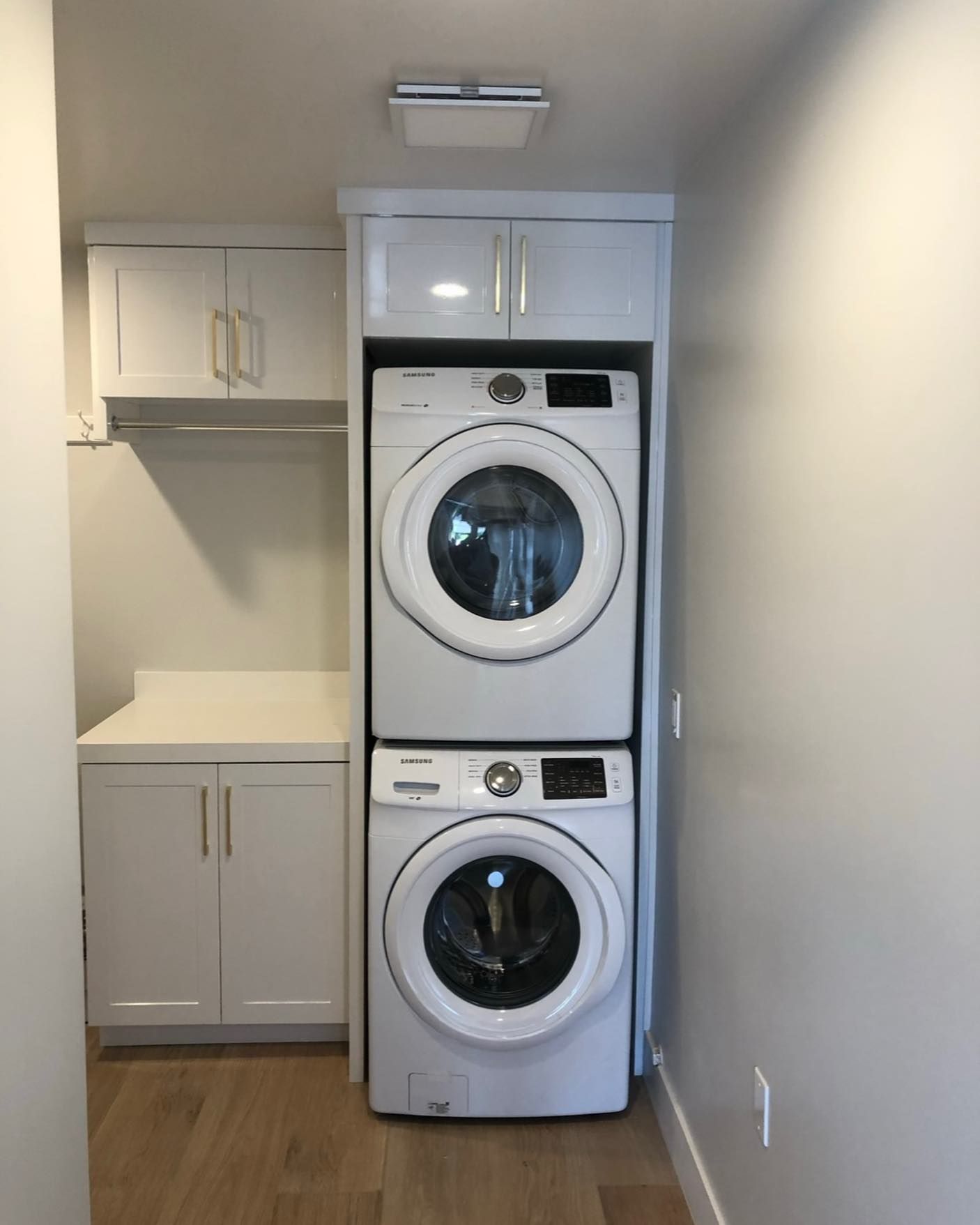 Stacked washer and dryer in a small white laundry closet with cabinets and wood floor
