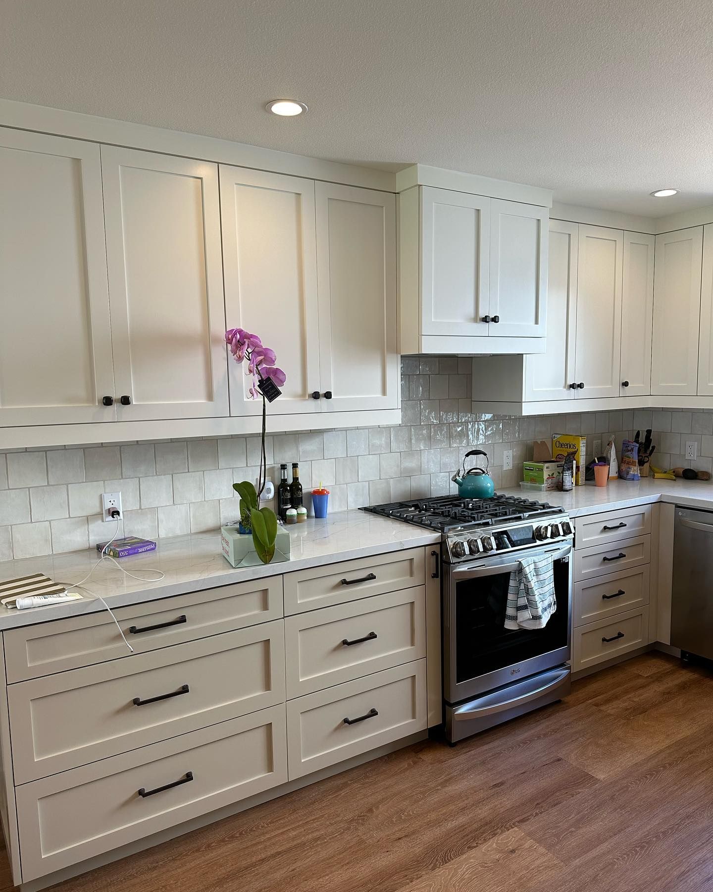 Bright white kitchen with cabinets, subway tile, stainless stove, and orchid on the counter