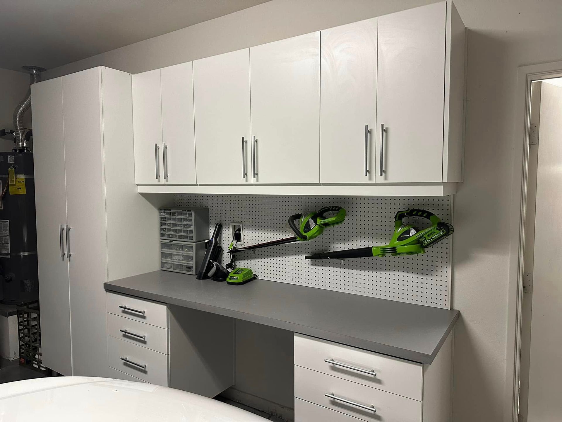 Garage workbench with white cabinets, gray countertop, pegboard, and green power tools.
