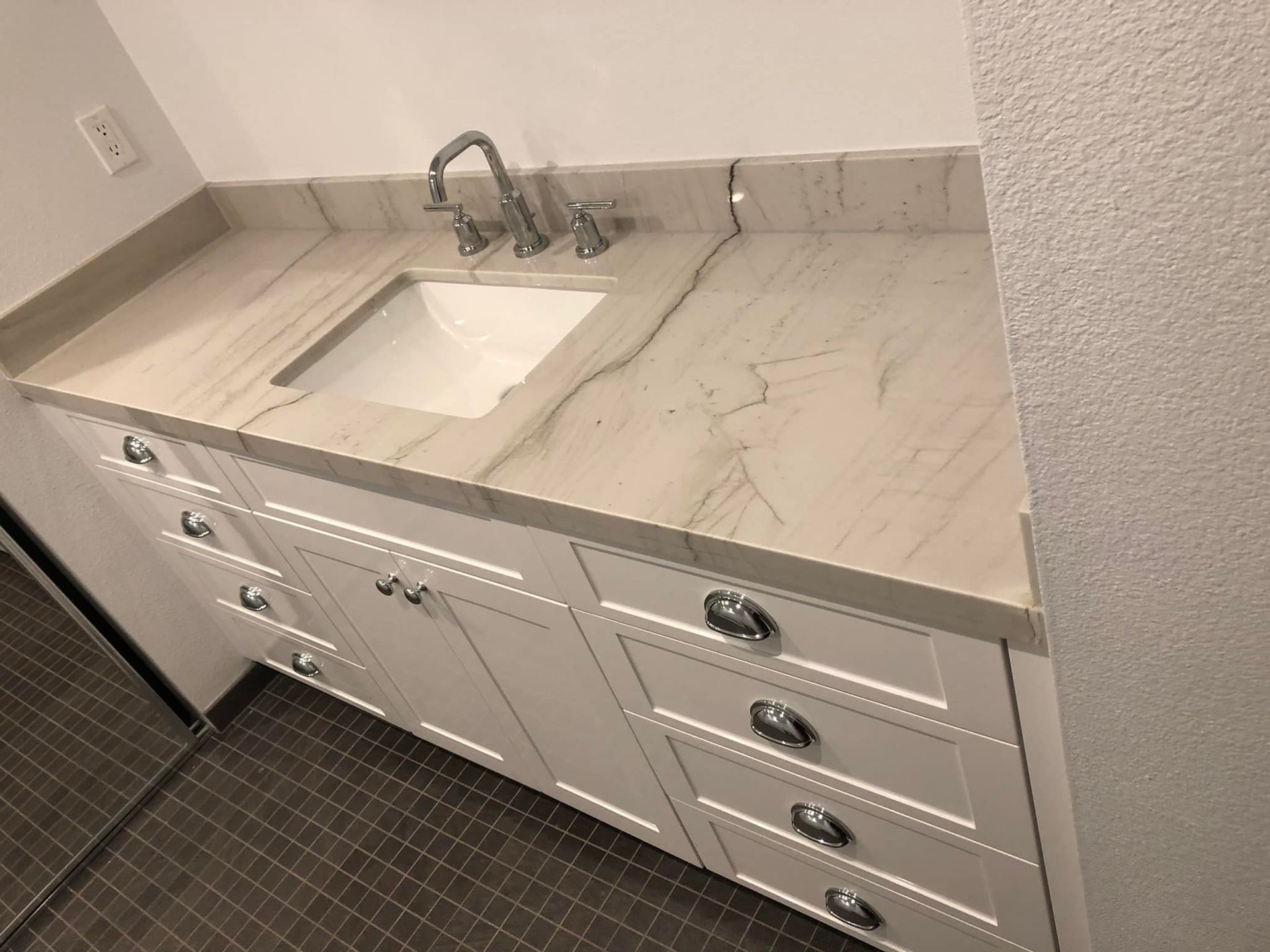 White bathroom vanity with marble-look countertop, built-in sink, and drawers on a tiled floor.