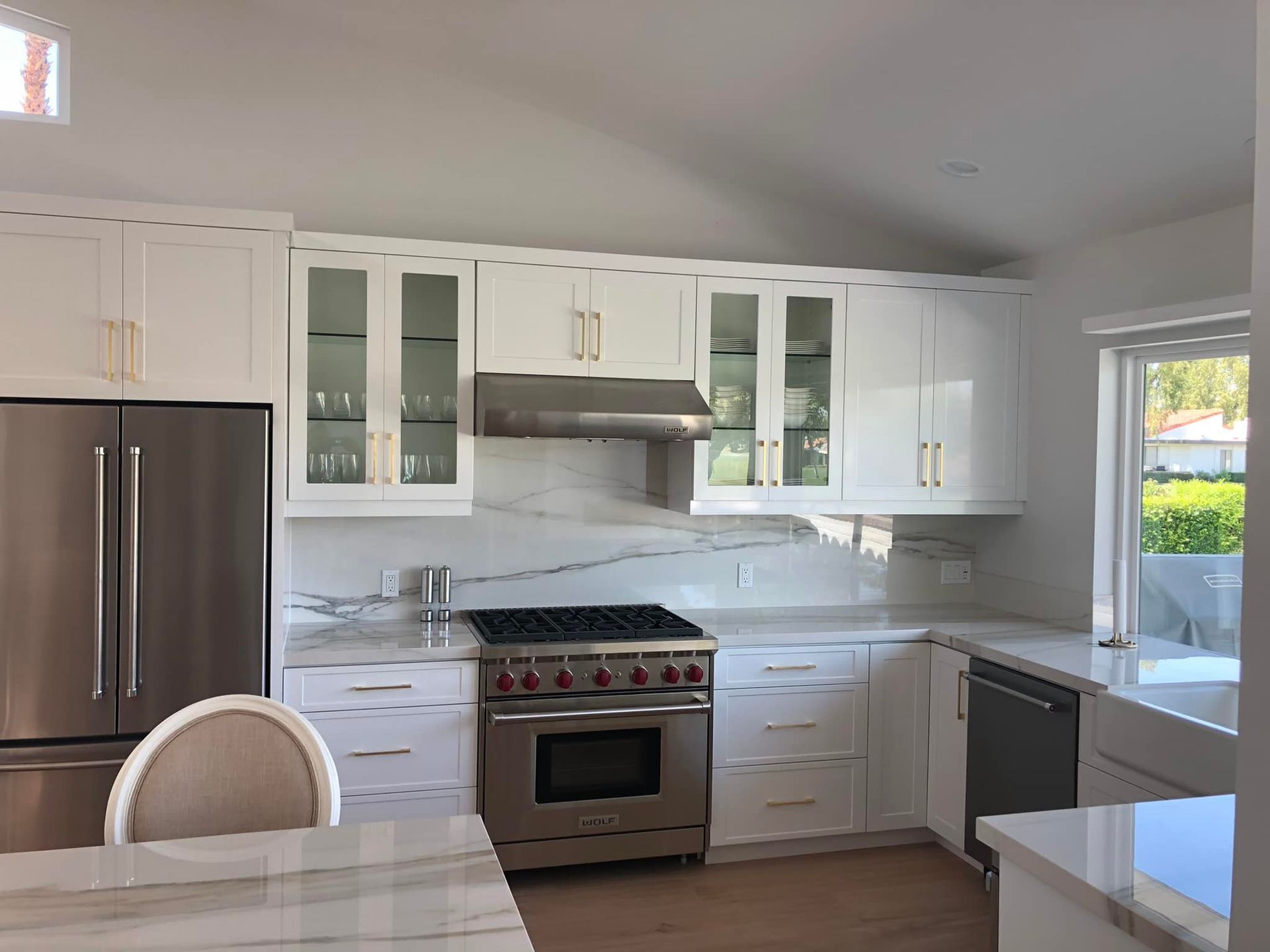 Bright modern white kitchen with stainless steel appliances, marble backsplash, and large window.