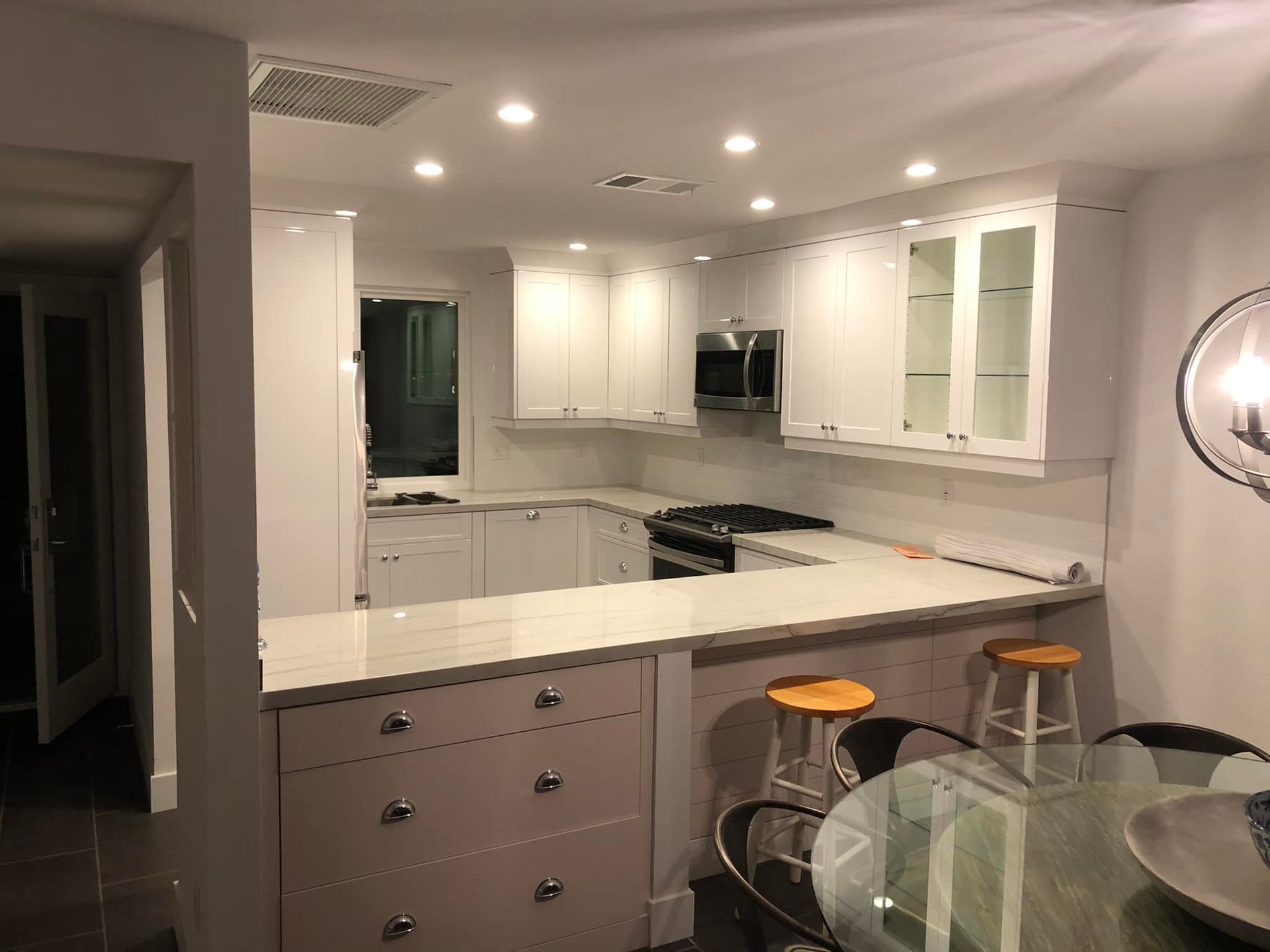 Modern white kitchen with island, gray cabinets, bar stools, and glass dining table