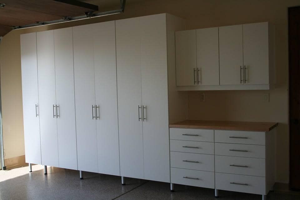 White storage cabinets and drawers along a wall in a room, with a small upper cabinet to the right.