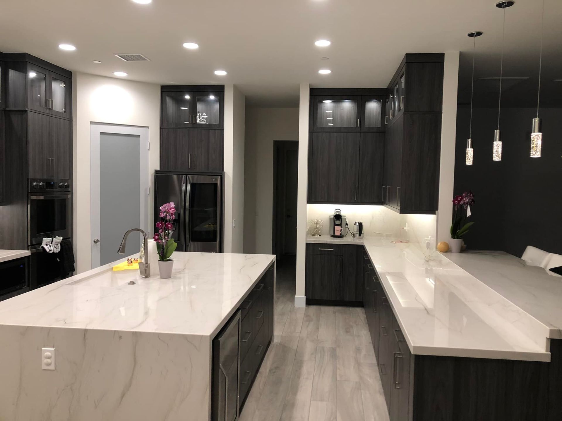 Modern kitchen with dark cabinets, white marble island and countertops, pendant lights, and stainless appliances