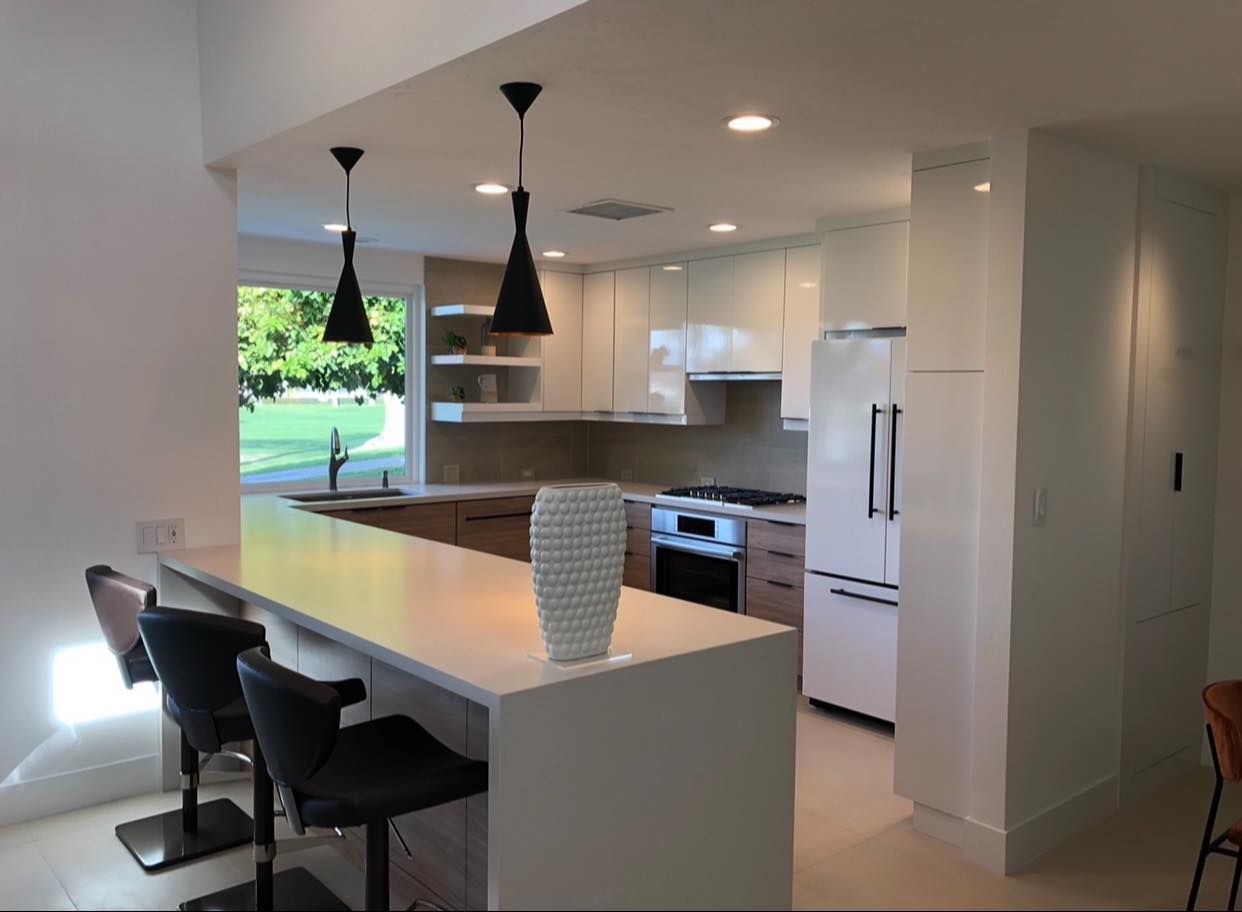 Modern white kitchen with island, black pendant lights, dining chairs, and green backyard view