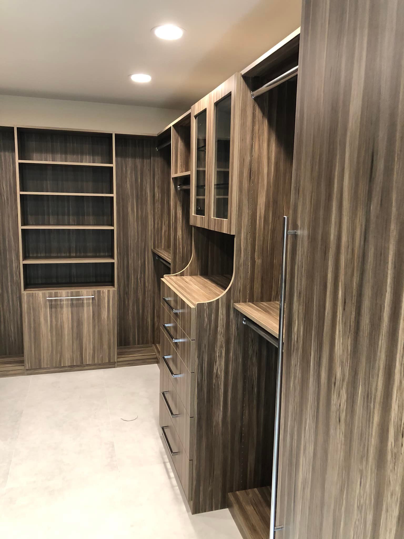 Built-in wooden walk-in closet with shelves, drawers, and hanging rods under recessed ceiling lights.