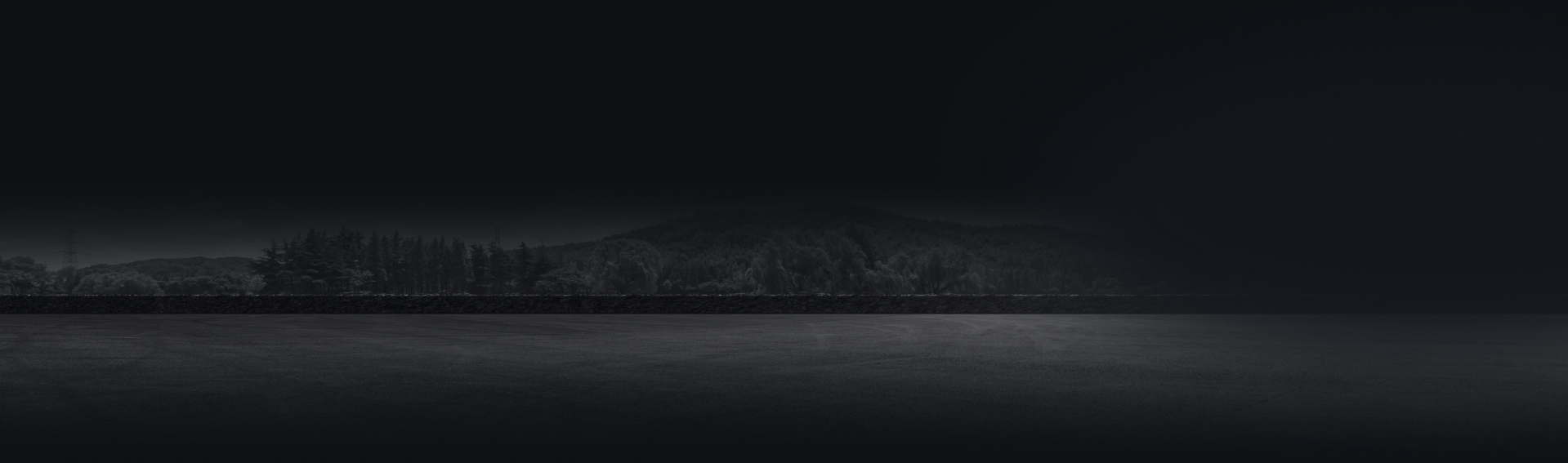 Dark, minimalist landscape featuring a body of water and a silhouetted shoreline under a cloudy sky.