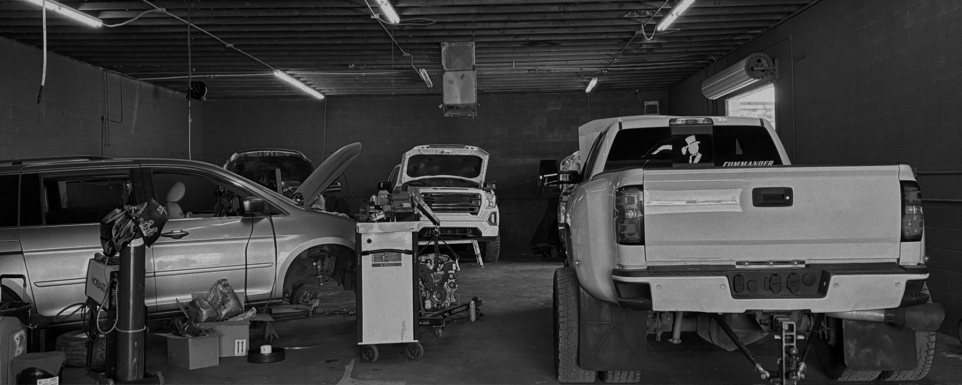 A black and white photo of a car repair shop with vehicles undergoing service.