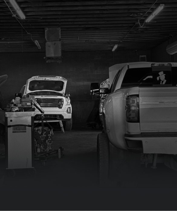 Trucks in a dim garage; one with hood open, a wheel alignment machine in view.