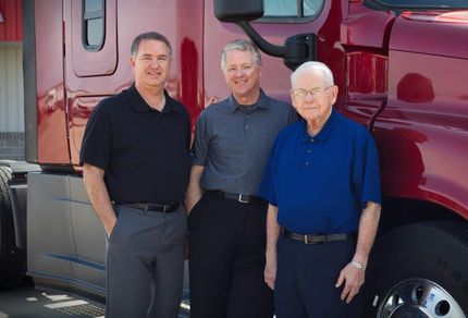 Three men are posing for a picture in front of a red truck.