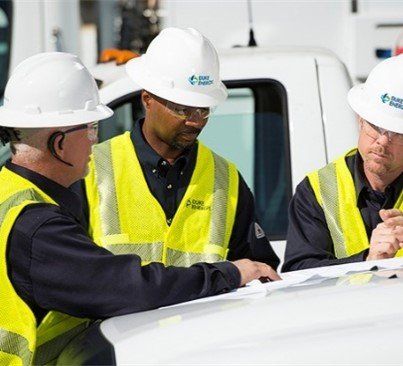 Three men wearing hard hats and yellow vests are looking at a blueprint