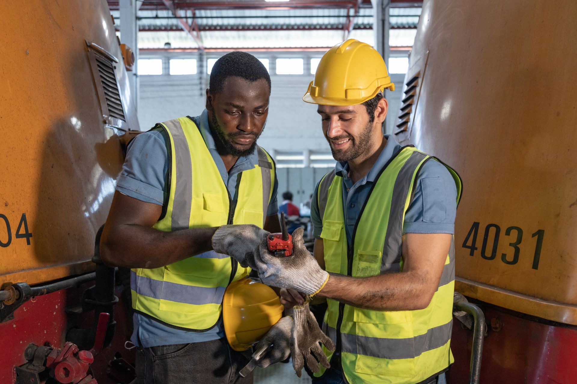 Two construction workers are working on a train in a factory.