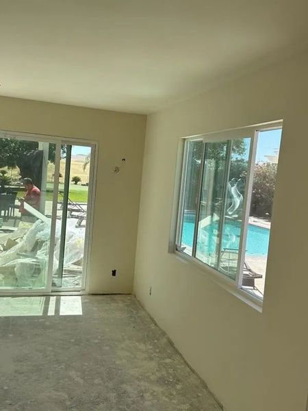Empty room with a sliding glass door and window overlooking a pool; off-white walls and concrete floor.