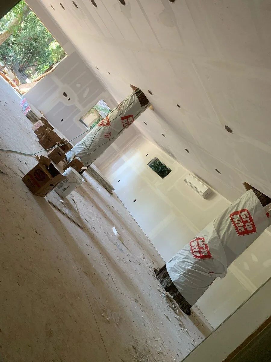 Interior construction site: finished drywall, covered columns, unfinished floor, and windows.