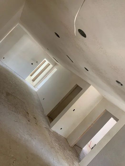 Interior of a room under construction; white walls, recessed lighting holes, rectangular openings, and a skylight.