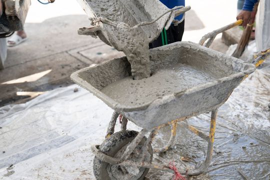 Wet concrete being poured into a wheelbarrow at a construction site