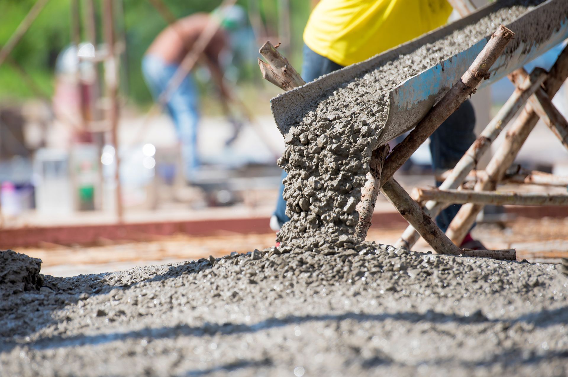 Concrete being poured at a construction site from a wheelbarrow onto a fresh slab.