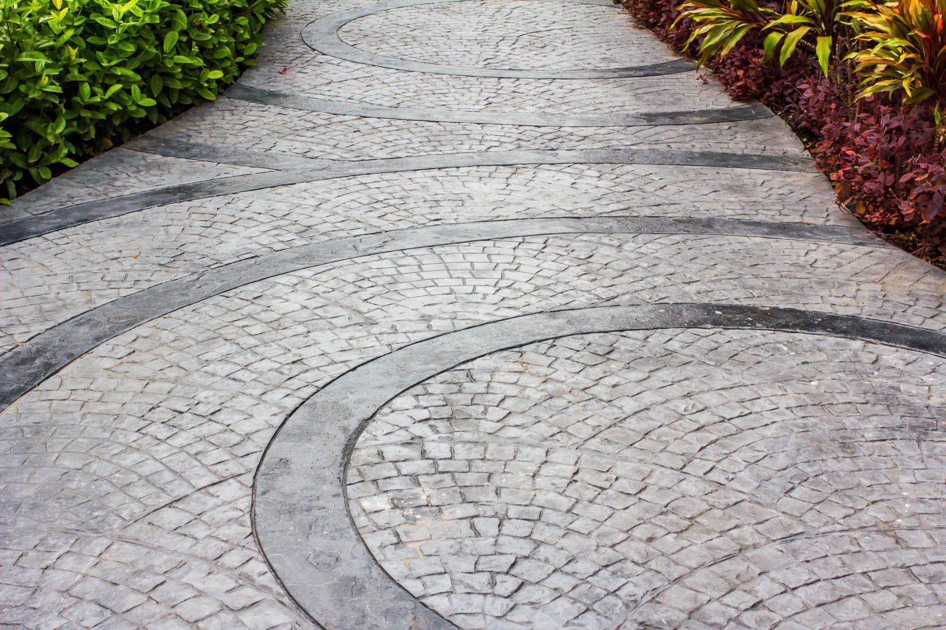 Curved stone garden path bordered by green and red shrubs