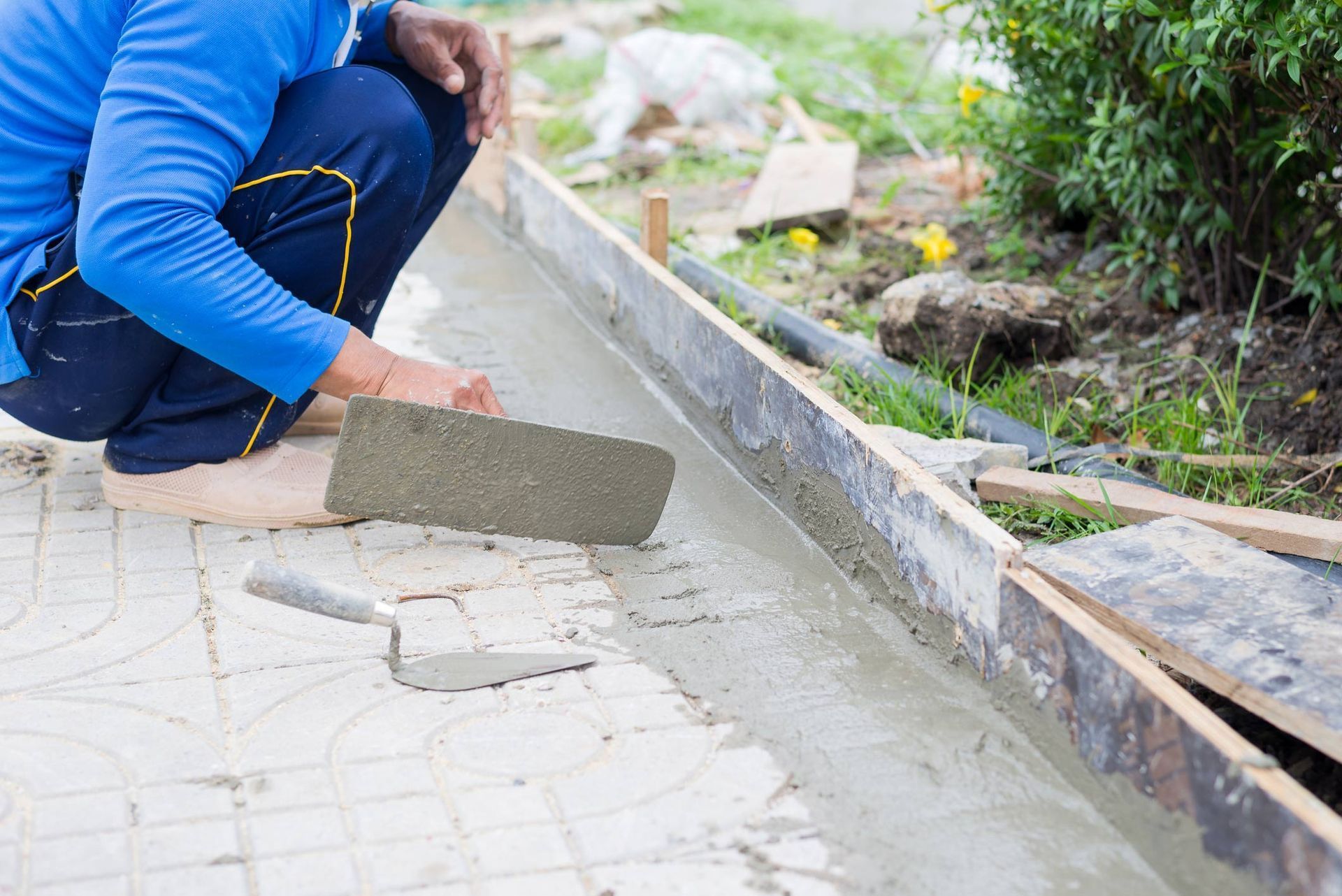 Worker spreading wet concrete along a curb with a trowel outdoors