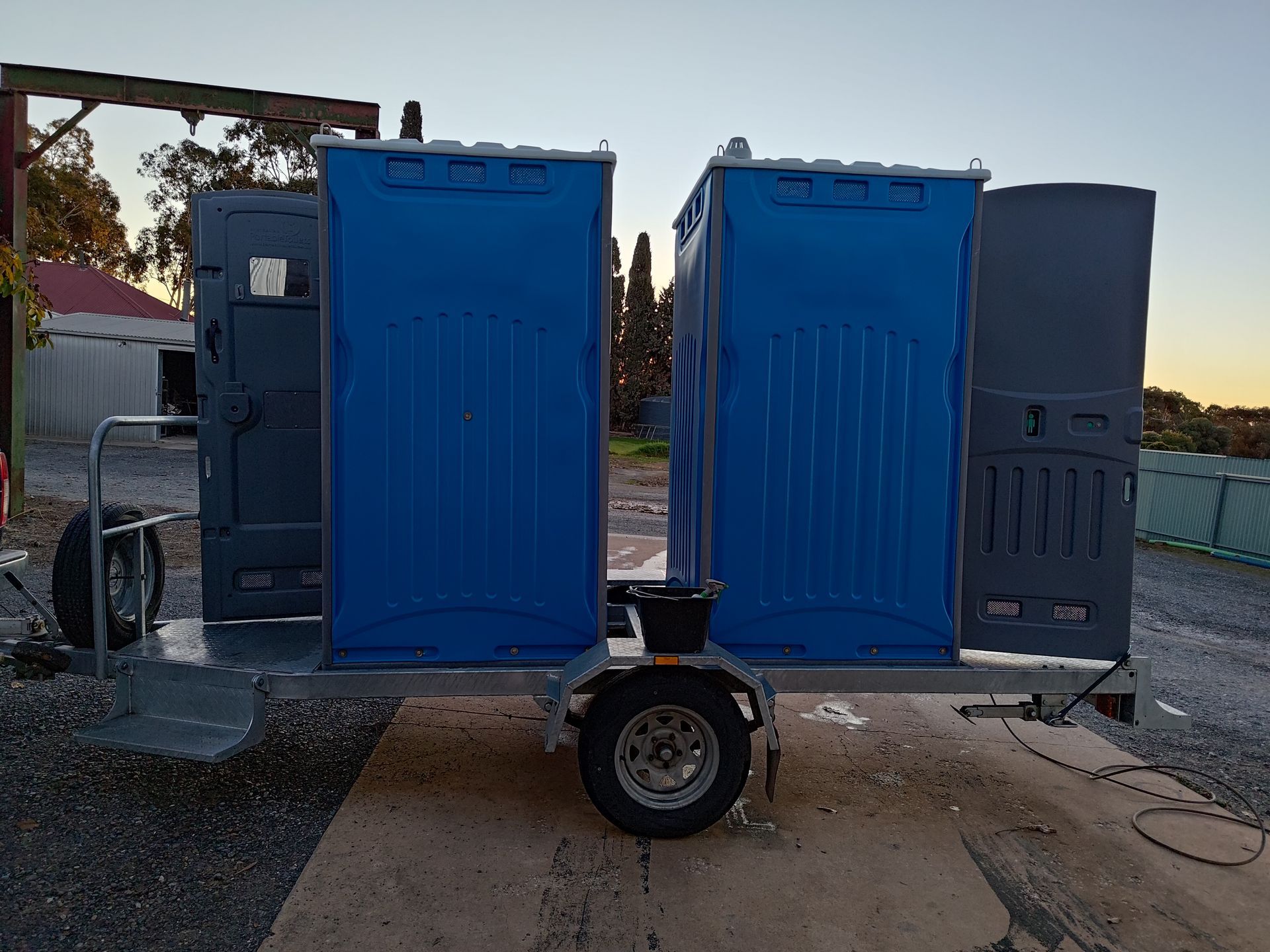 Portable toilets on a trailer, blue and gray, parked outdoors.
